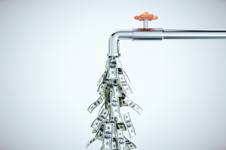 Water tap dripping dollar bills on gray background.